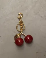 Llavero con dije de cerezas rojas brillantes y detalles en dorado.