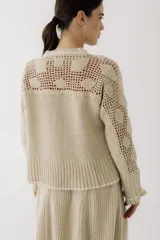 Saco de punto color beige, con diseño de calados en la parte superior y mangas, cierre frontal con botones y cuello redondo.