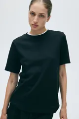 Remera de punto interlock pesado color negro, con cuello redondo ribeteado en canalé, mangas cortas y bajo recto.