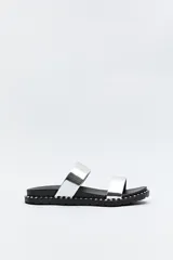 Sandalias planas plateadas con dos tiras anchas y suela negra con detalles metálicos.