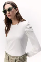 Remera de rib color crudo, con cuello redondo y mangas largas abullonadas y fruncidas en los hombros.