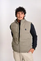 Chaleco puffer de corte regular, color beige, con cierre frontal y cuello alto. Presenta un diseño acolchado horizontal y logo bordado en el pecho.