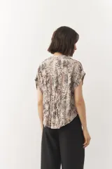 Blusa corta de manga corta con estampado en blanco y negro, cuello mao y cierre frontal con botones. Cuenta con detalle de elástico fruncido en la cintura que genera un efecto peplum.