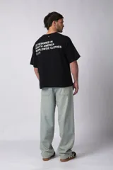 Remera de corte boxy y fit cuadrado, confeccionada en algodón grueso de alta calidad. Presenta un diseño minimalista en el frente con un pequeño logo circular y una estampa de gran tamaño en la espalda con la frase 'Designed in South America, Worldwide Clothes'.