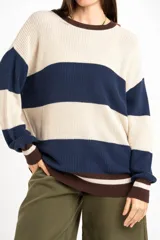 Sweater oversize de tejido de punto con diseño de rayas horizontales anchas en color beige y azul marino, cuello redondo marrón y puños y dobladillo en marrón con líneas beige y blancas.