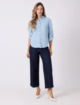 Camisa de algodón y lyocell, marca Weekend Routine, color celeste con finas rayas blancas. Tiene cuello con solapa, botones metálicos en la abertura frontal y mangas largas regulables con presilla y botón. La espalda presenta un canesú horizontal con un tablón central, y el bajo es asimétrico y redondeado.