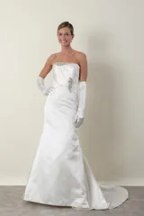 Vestido de novia largo color marfil, confeccionado en piel de ángel drapeada. Diseño strapless con apliques bordados en piedras en el escote, la cintura y la cola. Incluye guantes largos de satén blanco.