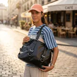 Bolso negro de cuero sintético con doble asa de hombro y correas decorativas frontales con hebillas metálicas. Incluye cierre superior y bolsillo interior.