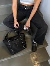 Bolso tipo tote bag de cuero negro con apliques metálicos plateados.