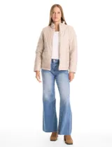 Campera 3 en 1 de color beige, con sistema de capas desmontables. La capa exterior es de tejido técnico resistente al viento y lluvia ligera, con capucha fija, cierre frontal con solapa, bolsillos de parche y ajuste elástico interno en la cintura. Incluye una campera interior capitoneada ultraliviana que puede usarse de forma independiente.