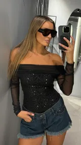 Body negro de manga larga con diseño off-shoulder. El cuerpo presenta una base de tul con lentejuelas brillantes, mientras que las mangas son de tul transparente.
