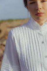 Camisa blanca de poplin de algodón con alforzas verticales y cuello alto estructurado. Mangas 3/4 con detalle de pliegues.
