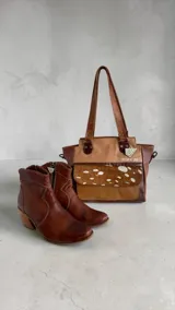 Cartera tipo tote de cuero en combinación de tonos marrones y beige, con diseño estructurado, doble asa de hombro, bolsillo frontal con solapa de pelo con estampado animal print, herrajes metálicos y llavero decorativo de la marca.
