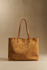 Bolso tipo tote de gran tamaño confeccionado en gamuza vegana color camel, con asas largas de cuero sintético a tono y placa metálica decorativa en el frente.
