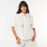 Camisa blanca de algodón de manga corta con cuello camisero, cierre frontal de botones y detalles de bordados calados con formas de estrellas de mar y soles.