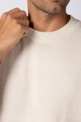 Remera de punto color crema, de manga corta, con cuello redondo acanalado y corte oversize.