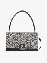 Cartera bandolera Tommy Hilfiger de diseño estructurado, confeccionada en jacquard con monogramas TH en tonos azul marino y beige, combinada con detalles en cuero sintético negro. Cuenta con solapa frontal, cierre metálico con logo, asa superior y correa extraíble.