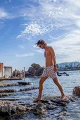 Short de baño con estampado geométrico abstracto en tonos azul, naranja y gris sobre fondo blanco. Cuenta con cintura elástica, bolsillos laterales y bolsillo trasero.