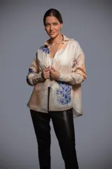 Camisa de batista blanca de corte oversize, con diseño estampado de tigres y flores en tonos azul y naranja. Presenta cuello camisero, mangas largas con puños anchos, espalda con tabla y ruedo irregular.