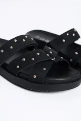 Sandalias negras de doble tira con tachas doradas, suela plana y diseño cómodo.