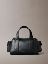 Cartera estructurada Calvin Klein de piel sintética negra, con diseño de asas superiores y bolsillos laterales. Cuenta con cierre de cremallera y logo metálico grabado en la parte delantera.