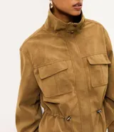 Campera Blue Steel de poliuretano con textura aterciopelada de efecto gamuza, color tostado. Cuenta con cuello alto, cierre frontal con solapa y botones a presión, bolsillos frontales con tapa y cordón ajustable en la cintura.