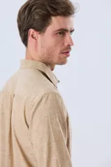 Camisa de lino de manga larga en color beige, con cuello camisero, cierre frontal de botones y un bolsillo ojal en el pecho.