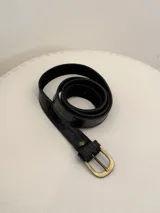Cinto de cuero negro con textura efecto cocodrilo y hebilla metálica en tono bronce.
