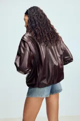 Chaqueta de diseño amplio en efecto piel color marrón oscuro, con cuello subido, mangas largas con puños, bolsillos laterales y bajo elástico. Cierre frontal con cremallera y solapa con botones a presión.