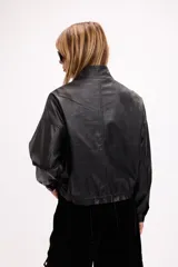 Campera corta de cuero sintético en color beige, con diseño de calce relajado, cierre frontal metálico, bolsillos con solapa en el frente y cordón ajustable en el ruedo.