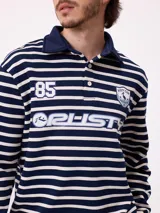Polo de manga larga con diseño a rayas horizontales en azul marino y blanco. Presenta cuello tipo polo con cierre de botones, estampado frontal con el logo de la marca y el número 85, y puños elásticos.