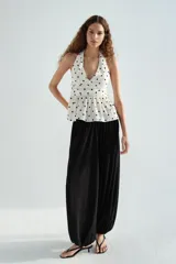 Top halter color blanco con estampado de lunares negros, escote en V pronunciado y detalle fruncido en la cintura con vuelo tipo peplum.