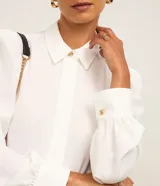 Camisa de crepé color blanco, con cuello inglés, manga larga abullonada con puños abotonados y cierre frontal oculto con botón diferenciado en el cuello.