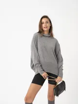 Sweater gris de tejido fino con cuello alto, silueta amplia y hombro caído.