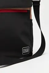 Cartera tote negra con doble asa superior y correa desmontable y regulable. Cuenta con un bolsillo frontal con solapa y cierre, y bolsillos laterales. Presenta pespuntes blancos decorativos y un logo cuadrado en la parte inferior.