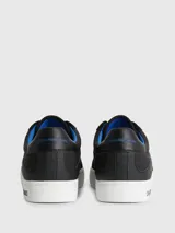 Zapatillas urbanas Calvin Klein con diseño de corte bajo. Presentan una combinación de materiales en la capellada, incluyendo paneles de nailon, cuero y ante en color negro. Destacan por su suela de goma blanca con el logo de la marca estampado en el lateral, forro interior en color azul vibrante y cierre mediante cordones.