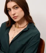 Conjunto de collar en capas de metal dorado, compuesto por una gargantilla rígida decorada con esferas y un dije central con forma de flor, y un collar largo de cadena fina con colgantes en forma de pétalos o hojas.