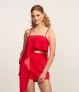 Blusa cropped de satén rojo con breteles finos, escote cuadrado y un llamativo volado asimétrico que cae lateralmente.