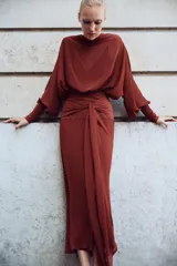 Vestido largo fluido en color bordó, confeccionado en georgette. Presenta cuello redondo, mangas largas con pliegues terminadas en puños y tiras ajustables para atar en la cintura. Incluye forro interior a tono.