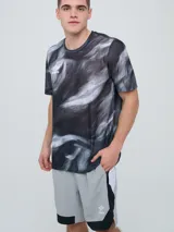 Remera deportiva Umbro modelo Niso, de manga corta y cuello redondo, con estampado abstracto en tonos negro y gris, y logo de la marca impreso en el pecho.