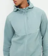 Buzo de fleece color verde agua con capucha ajustable, cierre frontal completo y bolsillo con cierre en el pecho. Presenta un diseño funcional con recortes en tejido plano y calce regular.