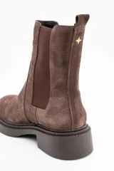 Bota tipo Chelsea de caña media, confeccionada en gamuza color marrón. Presenta paneles laterales elásticos al tono y una suela de goma robusta con plataforma baja y taco cuadrado.