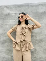 Blusa estampada con hojas verdes y blancas, con escote en V y mangas cortas abullonadas. Presenta volados en el ruedo y detalle de lazos en el frente.