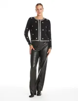 Chaqueta tejida de punto color negro, con cuello redondo y cierre frontal invisible. Presenta un diseño decorado con apliques de strass facetados y perlas en forma de flores y líneas en los bordes.