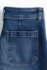 Jean de denim azul de corte acampanado y tiro alto, con bolsillos parche delanteros y traseros.