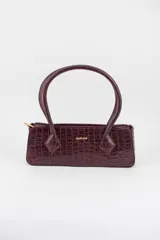 Cartera tipo baguette con textura símil cocodrilo, color bordó, de diseño alargado, con doble asa de mano y cierre superior. Presenta herrajes dorados y detalle de logo de la marca en el frente.