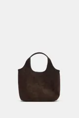 Bolso tipo mini shopper confeccionado en piel de ante color marrón oscuro. Presenta doble asa de mano integrada, cierre mediante botón imantado y bolsillo interior con cremallera.
