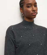 Suéter de punto color gris oscuro, de manga larga y cuello mediano estructurado, con patrón geométrico formado por líneas y aplicaciones de piedras brillantes.