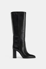 Bota alta de piel color negro, con caña alta, detalles de pespuntes verticales y tacón alto en bloque.