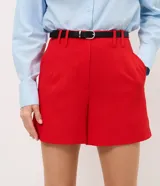 Short sastrero rojo de talle alto, con pinzas delanteras, cierre oculto y bolsillos traseros. Incluye un cinturón delgado de poliuretano.